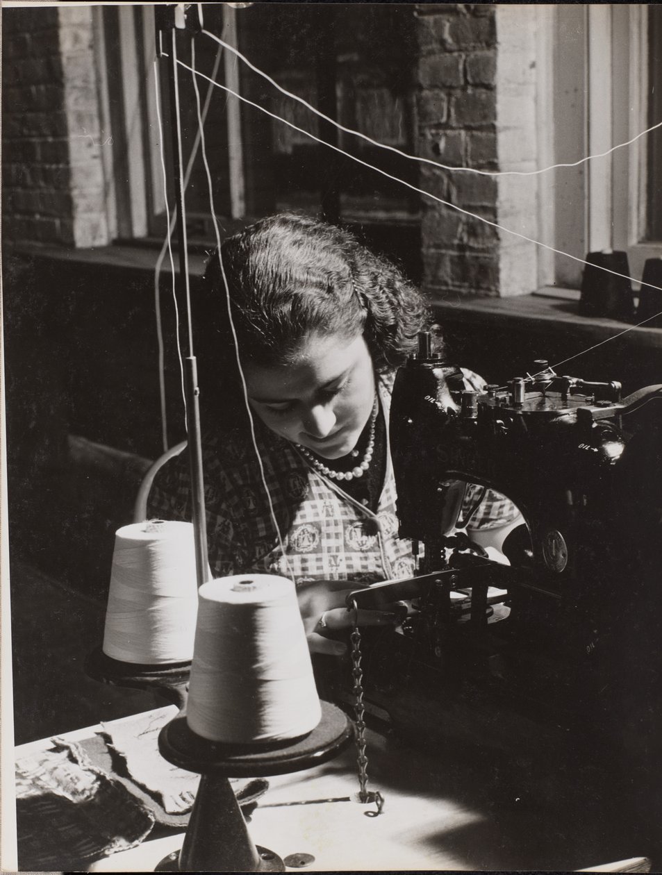 [Une femme utilise une machine à coudre enfilée à partir de deux bobines de fil blanc]. - Arnold Eagle