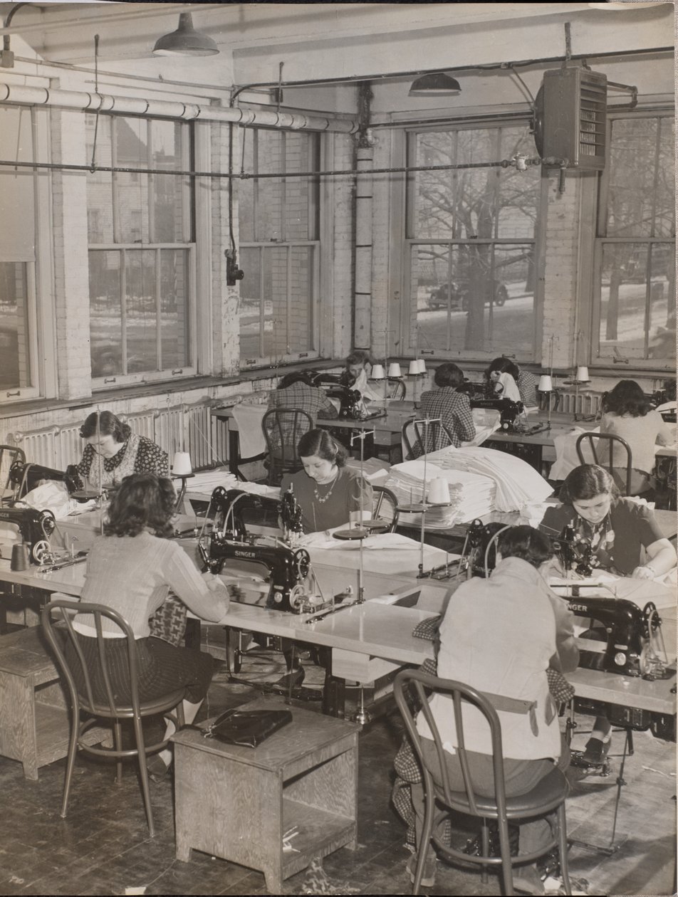 [Des femmes assises à des bureaux travaillent sur des machines à coudre]. - Arnold Eagle