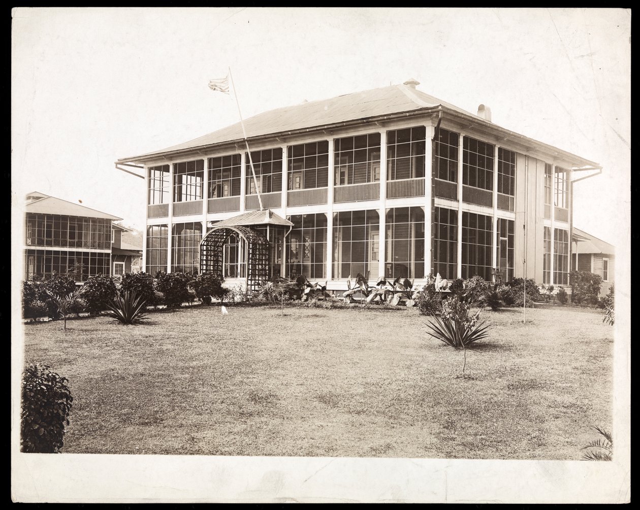 Maison à deux étages entourée de porches, avec un drapeau américain flottant; à Panama pendant la construction du canal, 1912 - Byron Company