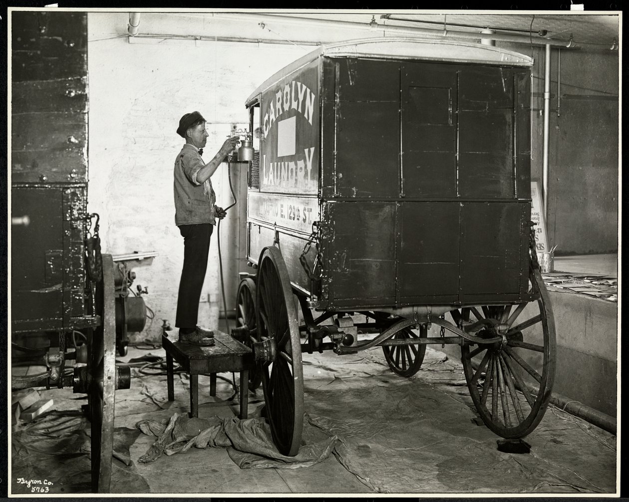 Un homme peignant au pistolet un wagon de livraison de Carolyn Laundry au 111 East 128th Street, East Harlem, New York, 1929 - Byron Company