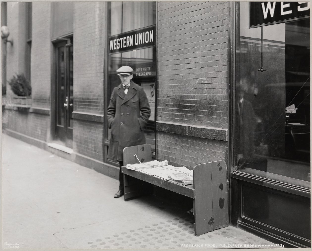 Le marchand de journaux aveugle, Frederick Rode, et le coin sud-est de Broadway et de la 41e Rue. Une enseigne Western Union est visible dans la fenêtre derrière M. Rode - Company Byron