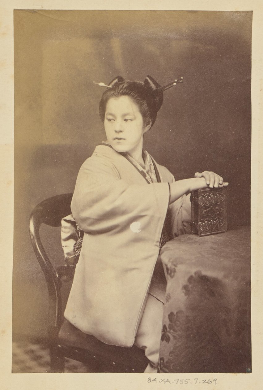 [Femme japonaise assise tenant un album de cartes-de-visite à une table]. - Felice Beato