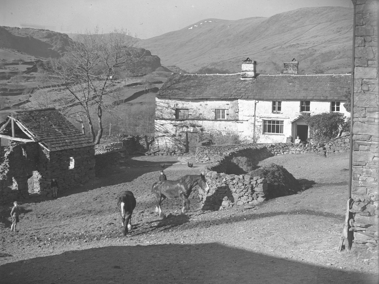 Trois jeunes garçons surveillant des chevaux dans la cour de ferme de Kentmere, avec la ferme et les montagnes derrière. - Joseph Hardman