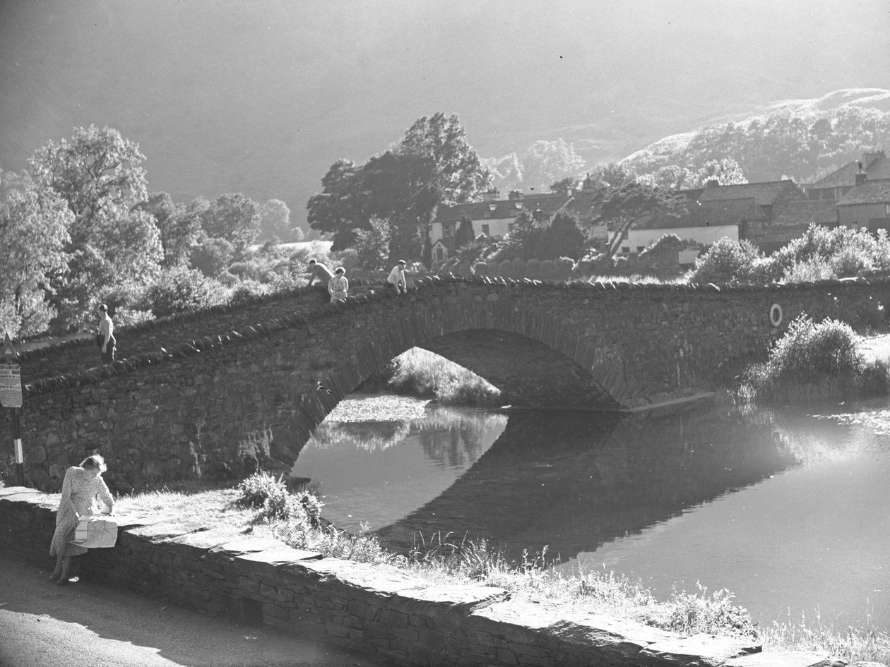Femme assise sur un mur étudiant une carte avec une rivière et un pont en pierre en arrière-plan - Joseph Hardman