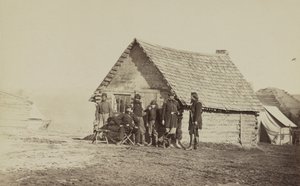 Un groupe de soldats et deux jeunes hommes, dont un afro-américain, devant des quartiers en cabane en rondins, 1861-65