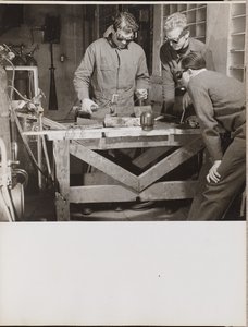 [Trois hommes portant des lunettes de protection soudent une pièce de métal sur une table].