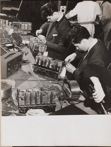 [Deux jeunes hommes portant des blazers travaillent sur des radios].