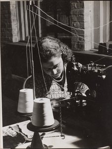 [Une femme utilise une machine à coudre enfilée à partir de deux bobines de fil blanc].