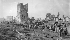 Une section de mitrailleuses australienne non identifiée avec des chevaux de bât passant devant les ruines de la Halle aux Draps. Notez plusieurs camions à moteur garés en arrière-plan, 19 octobre 1917 - Australian Photographer