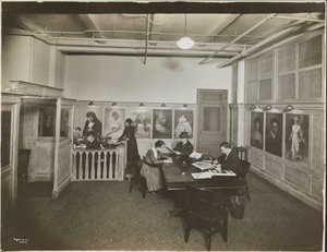 Bureau principal/salle de réception à la Mutual Film Co. avec secrétaire au bureau, personnes à une table lisant, et portraits sur le mur, New York