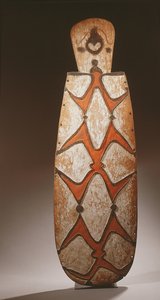Bouclier ovale Asmat, sculpté en relief avec des figures stylisées, un masque en haut