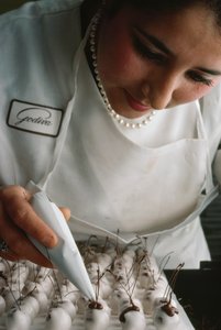 Un chef Godiva attache des tiges en chocolat à des cerises recouvertes de fondant. Bruxelles, Belgique.