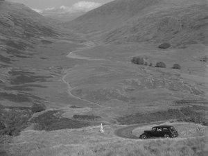 Une femme surplombe une vallée ouverte, avec une voiture garée à proximité. - Joseph Hardman