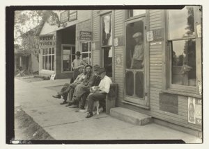 Hommes avec chien assis sur un banc devant un magasin général