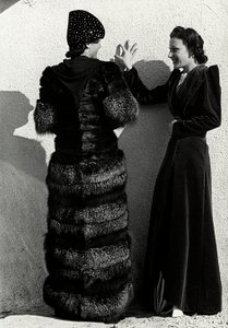Deux mannequins présentent des créations de la maison de couture italienne "Dragoni". Un mannequin vu de dos porte un manteau en renard argenté. L