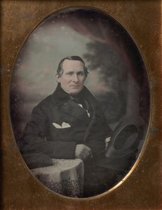 Homme portant un manteau et des gants, tenant un chapeau, assis devant un décor extérieur peint, années 1840 - Samuel Broadbent Jr..