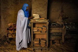 Homme feuilletant un manuscrit précieux dans sa maison sablonneuse, 2009 (photographie) - Unbekannter Künstler
