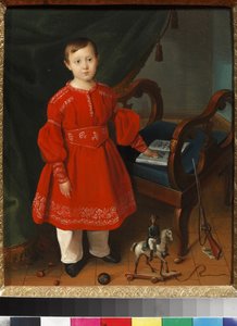 Portrait de petit garçon en robe rouge posant parmi ses jouets et un abécédaire