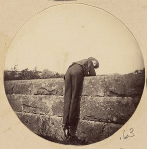 [Homme au chapeau penché sur un mur de pierre]