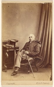 [Homme non identifié aux cheveux blancs, assis, tenant une canne, un chapeau haut de forme et un livre sur la table à gauche]. - W. and D. Downey