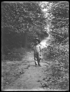 William Gray Hassler en chapeau de paille et salopette, portant une canne à pêche et un panier, marchant sur un chemin dans les bois - William Davis Hassler