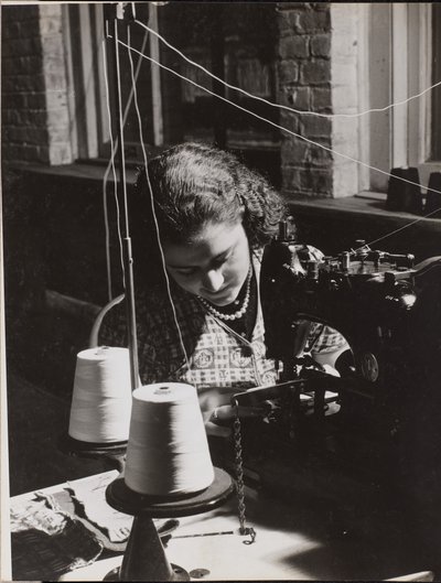 [Une femme utilise une machine à coudre enfilée à partir de deux bobines de fil blanc]. - Arnold Eagle