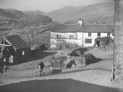 Trois jeunes garçons surveillant des chevaux dans la cour de ferme de Kentmere, avec la ferme et les montagnes derrière. - Joseph Hardman