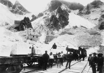 Excavateurs devant un convoi ferroviaire chargé de blocs de marbre à Ravaccione, dans les Alpes Apuanes (photo n/b)