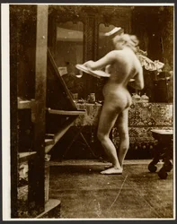 [Modèle de nu féminin debout dans un studio, tenant un carnet de croquis]
