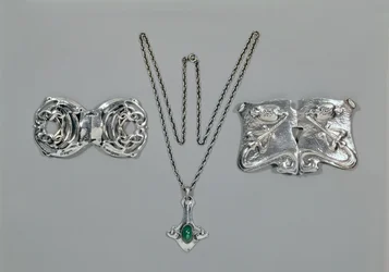 Bijoux en argent conçus pour Liberty. De gauche à droite : Fermoir de taille avec design celtique entrelacé, 1904. Pendentif et chaîne sertis de chrysoprase cabochon. Fermoir de taille avec design repoussé sur martelé