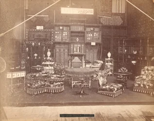 Exposition de S. Howard & Sons - Bâtiment principal, collection de meubles, y compris des chaises rembourrées, des tables, une cheminée, des armoires et des étagères. Sur les murs, des tapis, et sur les tables et étagères, des vases