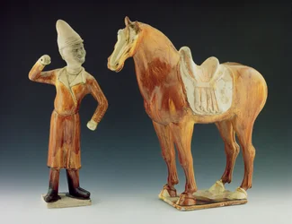 Figure de groom portant un manteau et un chapeau à visière avec un cheval sellé, dynastie Tang 618-906