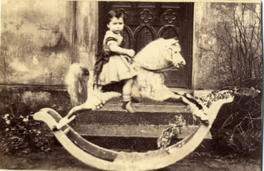Petite fille sur un grand cheval à bascule dans un jardin, années 1860