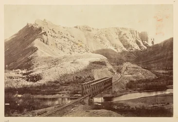 Vues sur le chemin de fer du Pacifique, de la voie ferrée traversant une rivière sur un pont en treillis, avec des montagnes au-delà