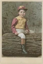 Petit garçon en tenue de jockey assis sur une bûche