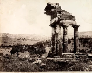 Vue des quatre colonnes restantes soutenant un entablement du Temple de Castor et Pollux dans la Valle dei Templi, Agrigente. Un panorama de la ville est visible à l