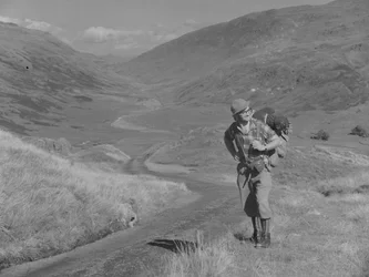 Un homme marchant avec un sac à dos sur le dos dans un paysage de vallée ouverte.