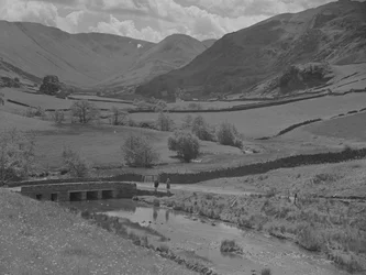 Vue sur un pont, un ruisseau, des champs et des montagnes.