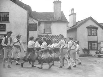 Hommes et femmes dansant à Hawkshead avec une enseigne pour le "15 Century Café" derrière et des commissaires-priseurs