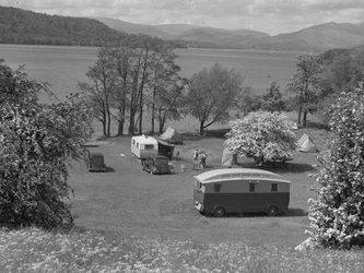 Tentes et caravanes installées dans un champ à Wastwater, lac et montagnes en arrière-plan