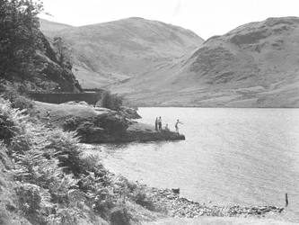 Trois hommes et une femme sur un affleurement rocheux dans le lac en train de pêcher, fells en arrière-plan