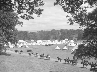 Vue de plusieurs tentes en forme de cône, à gauche ce qui semble être des hommes en uniforme à cheval (armée )