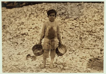 Manuel, 5 ans, migrant cueilleur de crevettes devant un tas de coquilles d