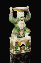 Bougeoir à glaçure œuf et épinard, modelé comme un immortel souriant avec une barbe en volutes, les bras levés pour soutenir l