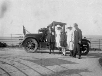 Un groupe de personnes devant leur voiture au bord de la mer, vers 1920