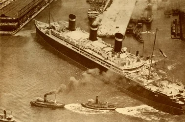 Photographie aérienne du Leviathan remorqué par de petits remorqueurs dans son dock à New York, vers 1930