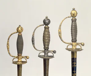 Poignées de trois épées françaises : une en acier, bleue et ornée de motifs en or ciselé, c.1730 ; une en acier percé et ciselé et le fond en or mat, c.1760 ; une en acier ciselé, gr