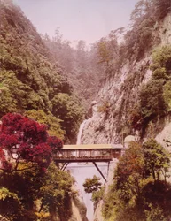 Pont couvert dans une gorge escarpée, avec des cascades en arrière-plan, Japon, vers 1890-1910